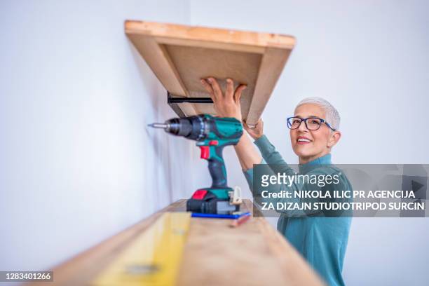 mature woman hanging shelf in apartment. - building shelves stock pictures, royalty-free photos & images