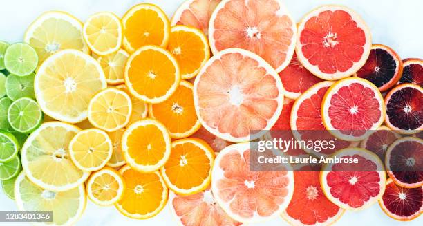 flat lay of rainbow of vibrant citrus fruit slices on white - agrumi foto e immagini stock