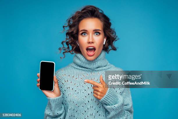 beautiful surprised woman standing in front of blue background with smart phone - disbelief stock pictures, royalty-free photos & images
