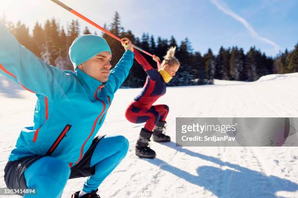 close-up of a young man and woman while warming up at a ski slope. overhead squat warming up - nordic skiing event stock pictures, royalty-free photos & images