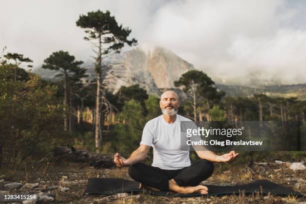 male senior practicing yoga outside with mountain view. praying and meditating alone. health and harmony with nature. - guru stock-fotos und bilder