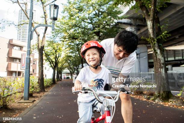 a boy learning how to ride a bike from his father - 日本人　応援 ストックフォトと画像