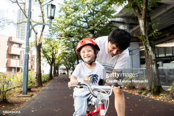 a boy learning how to ride a bike from his father - asian smiling father son stock pictures, royalty-free photos & images