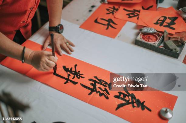 hand von asiatischen chinesischen männlichen üben chinesische kaligraphie für kommende chinesische neujahrsfeier hausdekoration zweck mit wohlstand und gute formulierung durch das schreiben es auf einem roten stück papier - chinesisches schriftzeichen stock-fotos und bilder