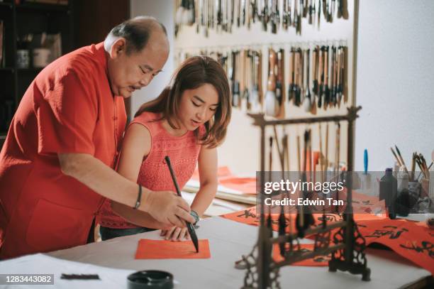 aziatische chinese vader die chinese kalligrafie voor chinees nieuwjaar fai chun (gunstige berichten) uitoefent en zijn dochter onderwijst door het op een stuk rood document te schrijven dat haar hand houdt - 55 year old male stockfoto's en -beelden