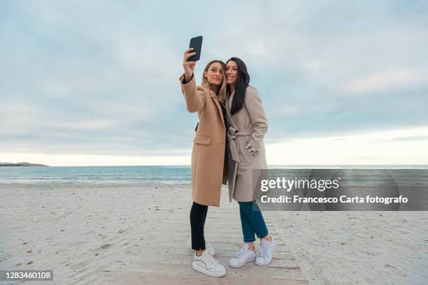 women taking selfie at the beach in autumn - autumn friends coats stock pictures, royalty-free photos & images