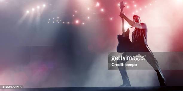 rock star holding up guitar on stage - rock music stock pictures, royalty-free photos & images
