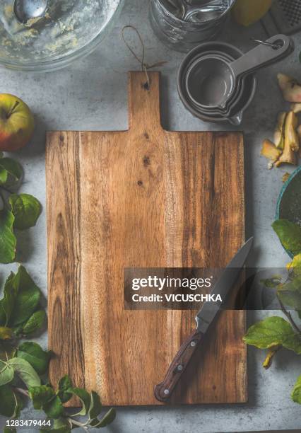 empty wooden rustic cutting board background on rustic table with fresh apples on branches, kitchen utensils and bake tools - food background stock-fotos und bilder