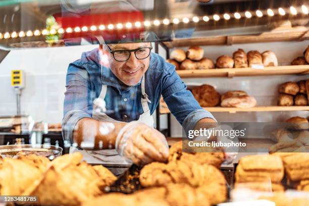 mann arbeitet in einer bäckerei und serviert frische bäckerei aus dem vitrinenschrank - bakery display stock-fotos und bilder