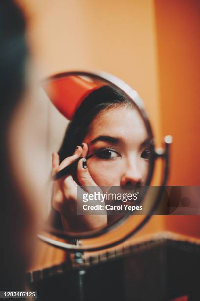 young female in evil costume putting some makeup for halloween in domestic bathroom - halloween makeup stock-fotos und bilder