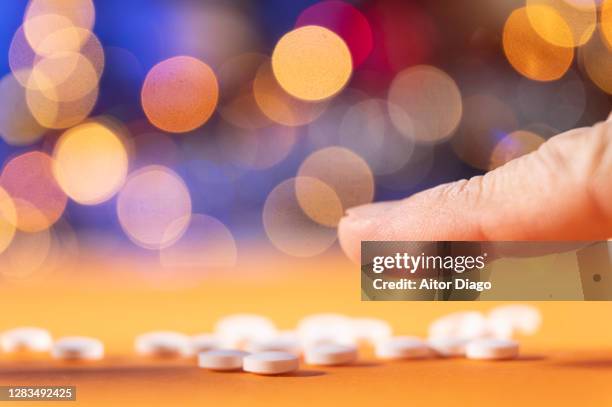 index finger of a man is going to take pills on a table. colorful lights in the background. - slaappil stockfoto's en -beelden