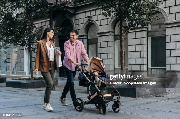familie met baby in een wandelwagen die onderaan de stad loopt - kinderkoets stockfoto's en -beelden