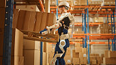 High-Tech Futuristic Warehouse: Worker Wearing Advanced Full Body Powered exoskeleton, Lifts Heavy Pallet full of Cardboard Boxes. Delivery Exosuit amplifies strength.