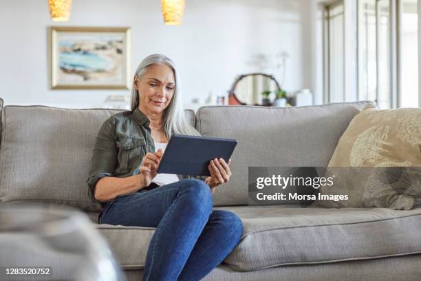 smiling mature woman using digital tablet at home - 50 59 years home stock pictures, royalty-free photos & images
