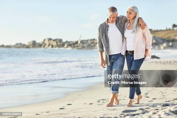 romantic couple in casuals walking at beach - 50 59 years stock pictures, royalty-free photos & images