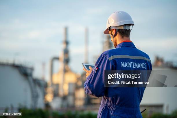 rear view of petroleum maintenance engineer working with digital tablet at oil and gas refinery facility visible in the background. sustainable energy concepts. - overalls stock-fotos und bilder