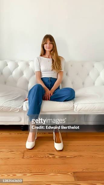 Bertille Canat wears a white t-shirt, blue flared denim jeans pants, white shoes, during an online fashion photo session via Apple Iphone / Facetime,...