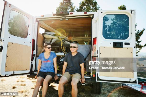 smiling couple sitting on back of van after windsurfing on summer afternoon - vorruhestand stock-fotos und bilder