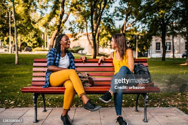 friends talking on bench - cross legged stock pictures, royalty-free photos & images