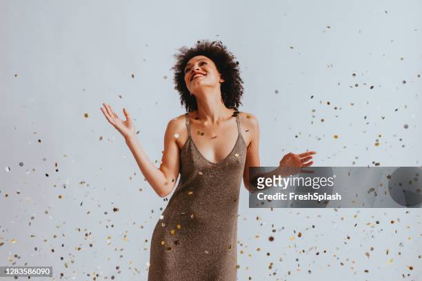 happy woman in a gold dress dancing under confetti - beautiful woman stock pictures, royalty-free photos & images