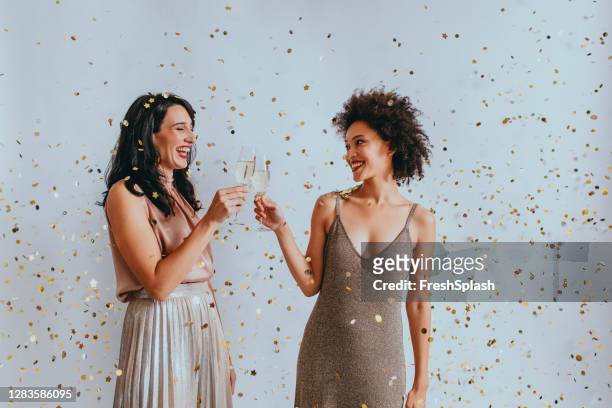 twee gelukkige vrouwen die de vooravond van het nieuwe jaar met een geroosterde champagne onder confetti vieren - oudjaarsavond stockfoto's en -beelden