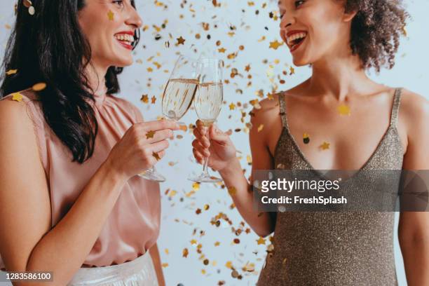 紙吹雪の下でシャンパントーストで大晦日を祝う2人の幸せな女性 - two year anniversary party ストックフォトと画像