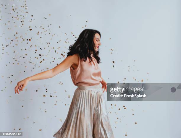 studio shopt einer schönen lächelnden eleganten frau tanzen mit konfetti geduscht - gray skirt stock-fotos und bilder