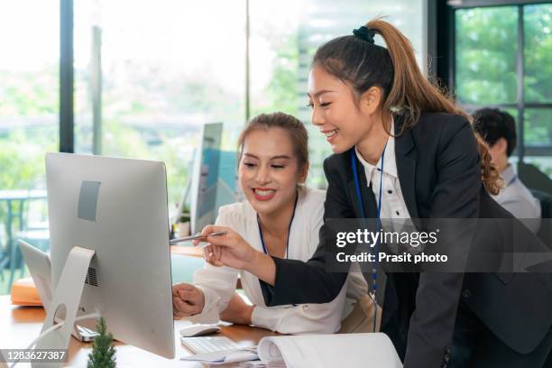 asian businesswoman manager using computer to discuss information with a younger woman colleague or new staff in a modern business desk. - stage performance foto e immagini stock