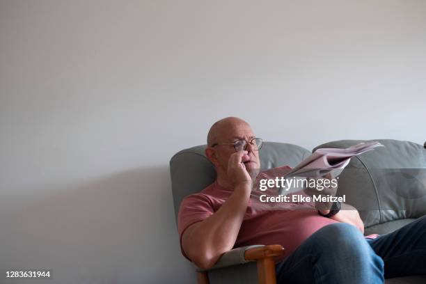 senior sitting on couch with newspaper - melbourne newspaper stock pictures, royalty-free photos & images