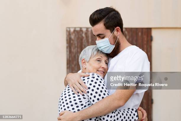 smiling older caucasian woman hugging young caucasian male nurse outside a house - hector vivas fotografías e imágenes de stock