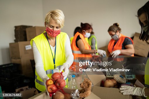 Vrouw met beschermend gezichtsmasker dat voedsel in een dakloze schuilplaats helpt verzamelen Vrouw met beschermend gezichtsmasker dat voedsel in een dakloze schuilplaats helpt verzamelen