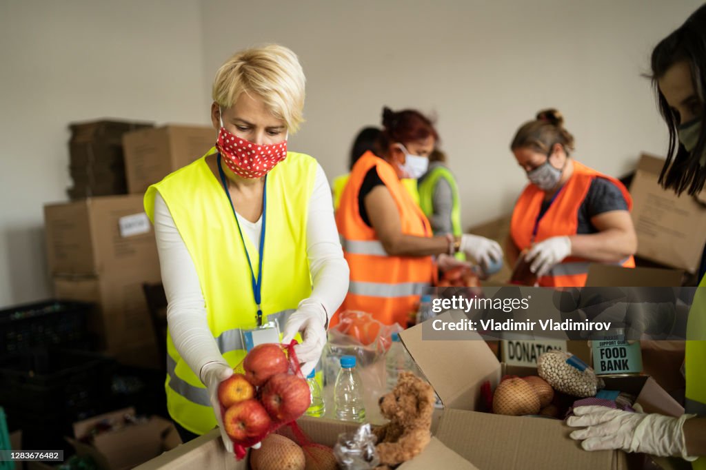 Woman with protective face mask helping collecting food in a homeless shelter