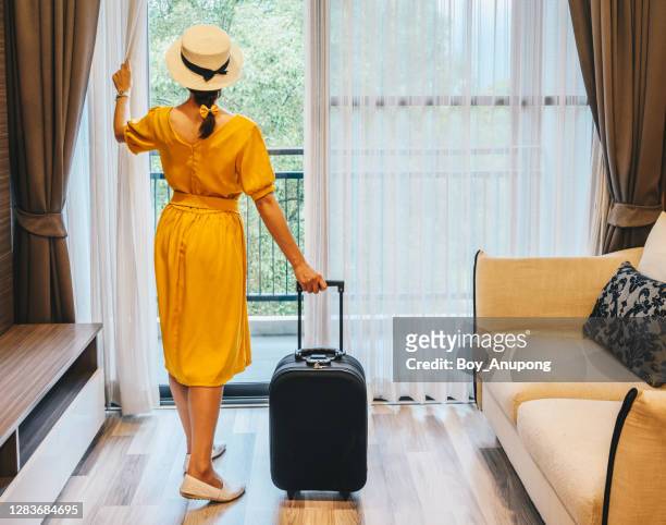 rear view of tourist woman standing nearly window, looking to beautiful view with her luggage in luxury hotel after check-in. - yellow suitcase stock pictures, royalty-free photos & images