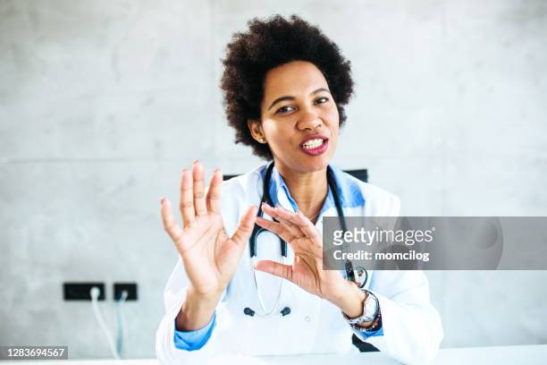 portrait of a female doctor talking at camera - black female doctor stock pictures, royalty-free photos & images