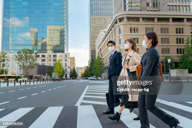 three business people crossing street while covering their faces with protective face masks - commuter mask stock pictures, royalty-free photos & images