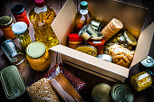 Cardboard box filled with non-perishable foods on wooden table. High angle view.