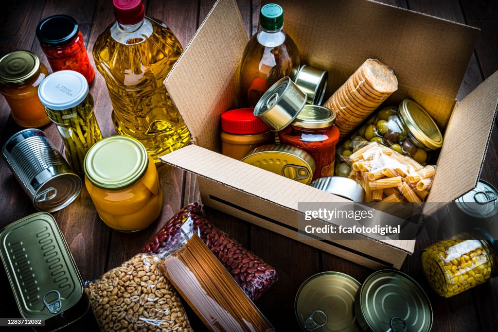 Cardboard box filled with non-perishable foods on wooden table. High angle view.