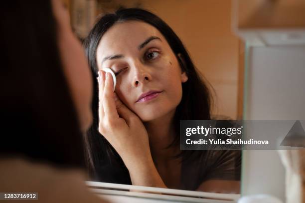 woman is removing mascara from lashes using white wipe cotton pad - maquillaje para ojos fotografías e imágenes de stock
