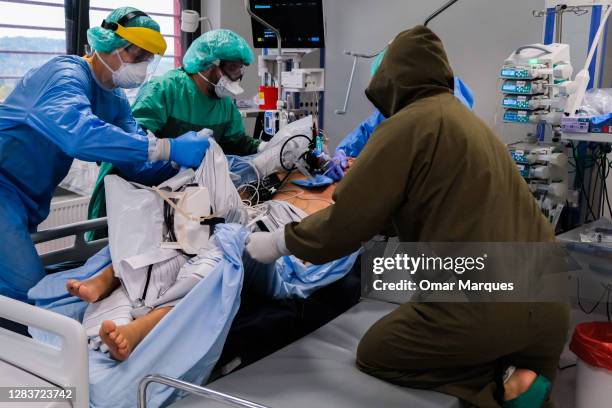 Medical personnel wear protective suits, masks, gloves and face shields as they transfer a patient for another bed to take for a tomography at the...