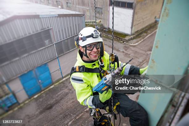 manual rope access technician - worker repairing tower - antenna in sunshine, holding drill in hand, preparing for work and looking to camera and smiling - abseiling stock pictures, royalty-free photos & images