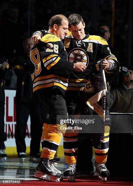 Andrew Ference of the Boston Bruins gives a jacket to recently retired Mark Recchi of the Bruins during a pregame ceremony on October 6, 2011 at TD...