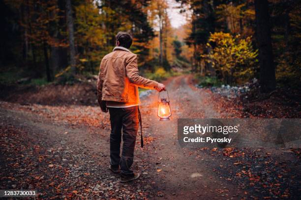 un homme avec une lanterne à un carrefour dans les bois - lanterne photos et images de collection