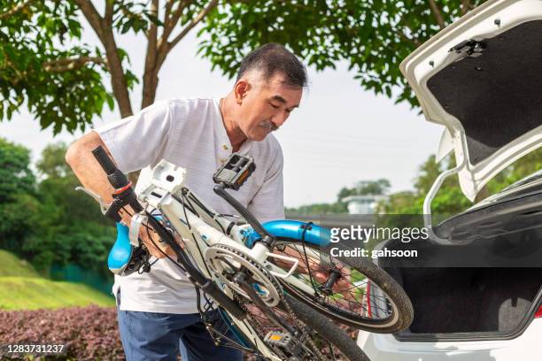 bejaarde die zijn fiets uit de boomstam van een auto neemt - geplooid stockfoto's en -beelden