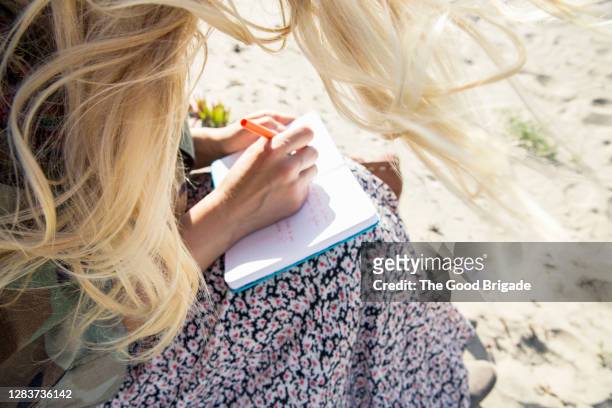 young woman writing in notebook on beach - strand of human hair stock pictures, royalty-free photos & images
