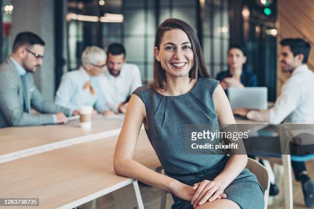 smiling businesswoman sitting in front of her colleagues - law office stock pictures, royalty-free photos & images
