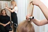 Hairstylist working on woman client with crimper