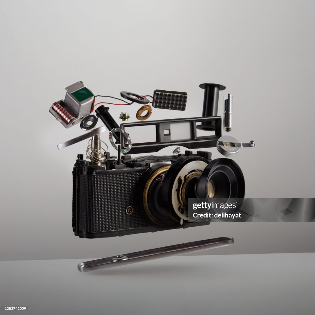 Teile und Komponenten einer zerlegten analogen Vintage-Filmkamera schweben datieren in der Luft auf weißem Hintergrund