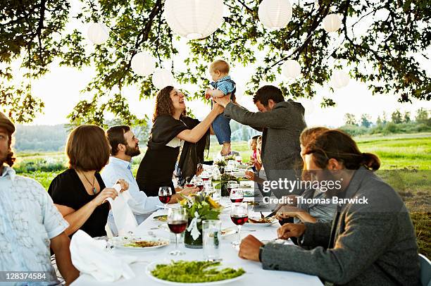 father handing baby to friend across table - raising baby stock-fotos und bilder