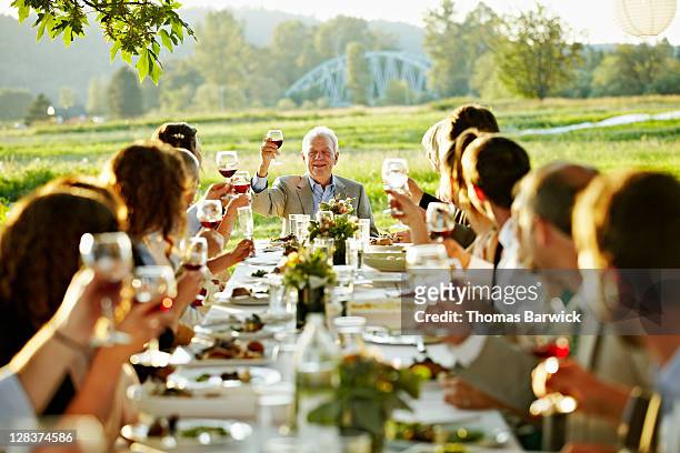 mature man sitting at head of table giving toast - festmahl stock-fotos und bilder