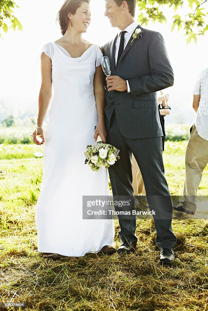 Bride and groom standing in field smiling